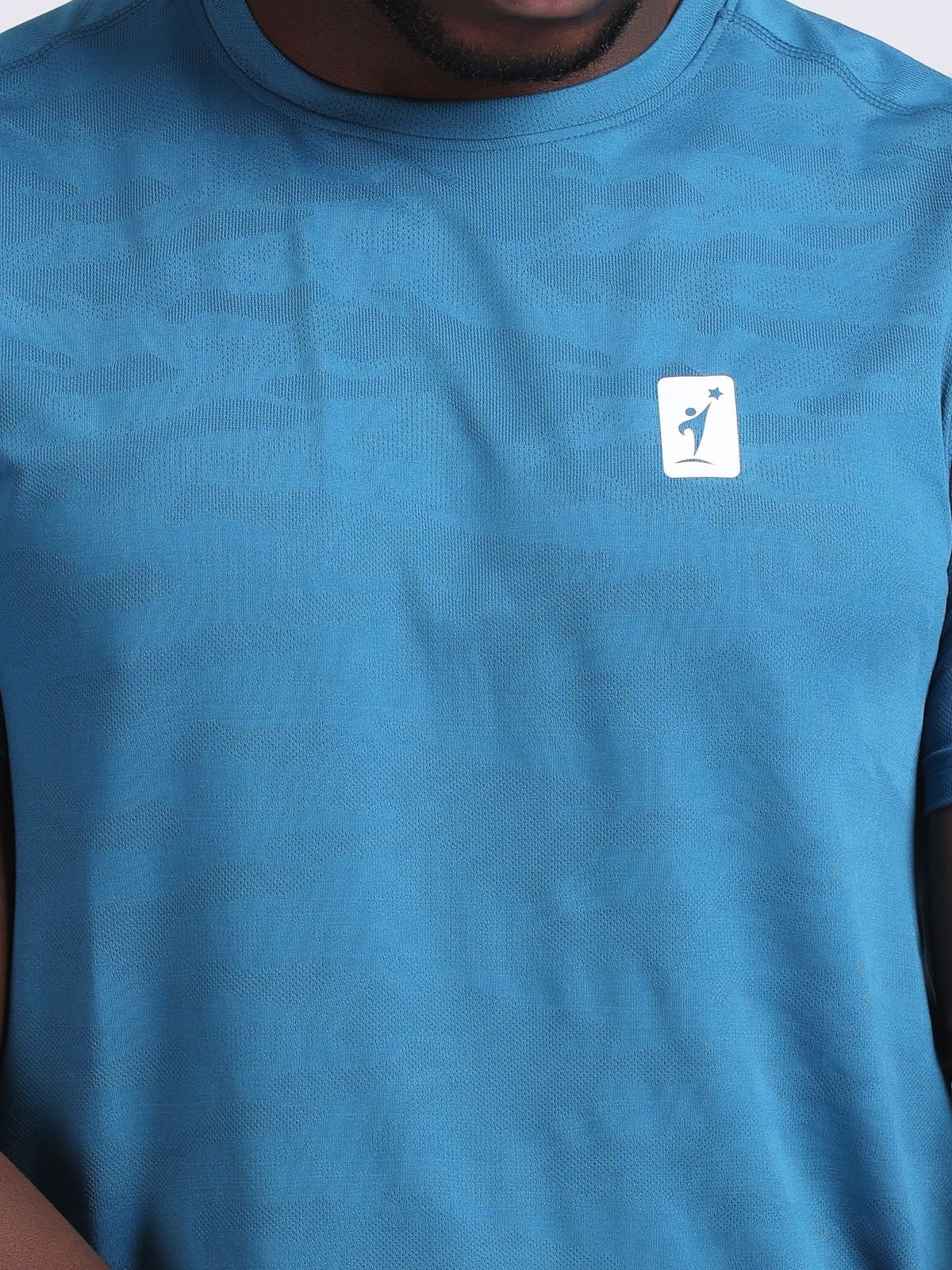 Close-up of the chest NDR SPORT logo on a teal JaqMesh activewear t-shirt.