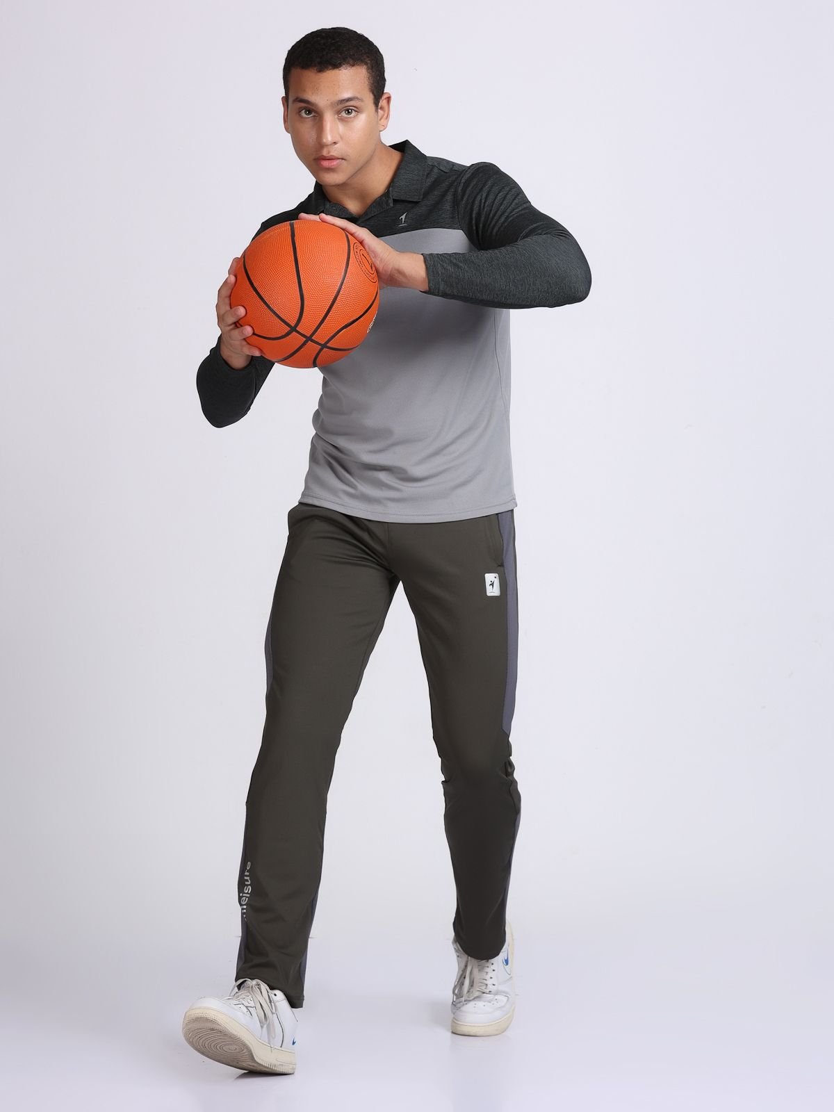 Full-body pose of a man holding a basketball while wearing a light grey and dark grey long-sleeve polo T-shirt SwanTech top.