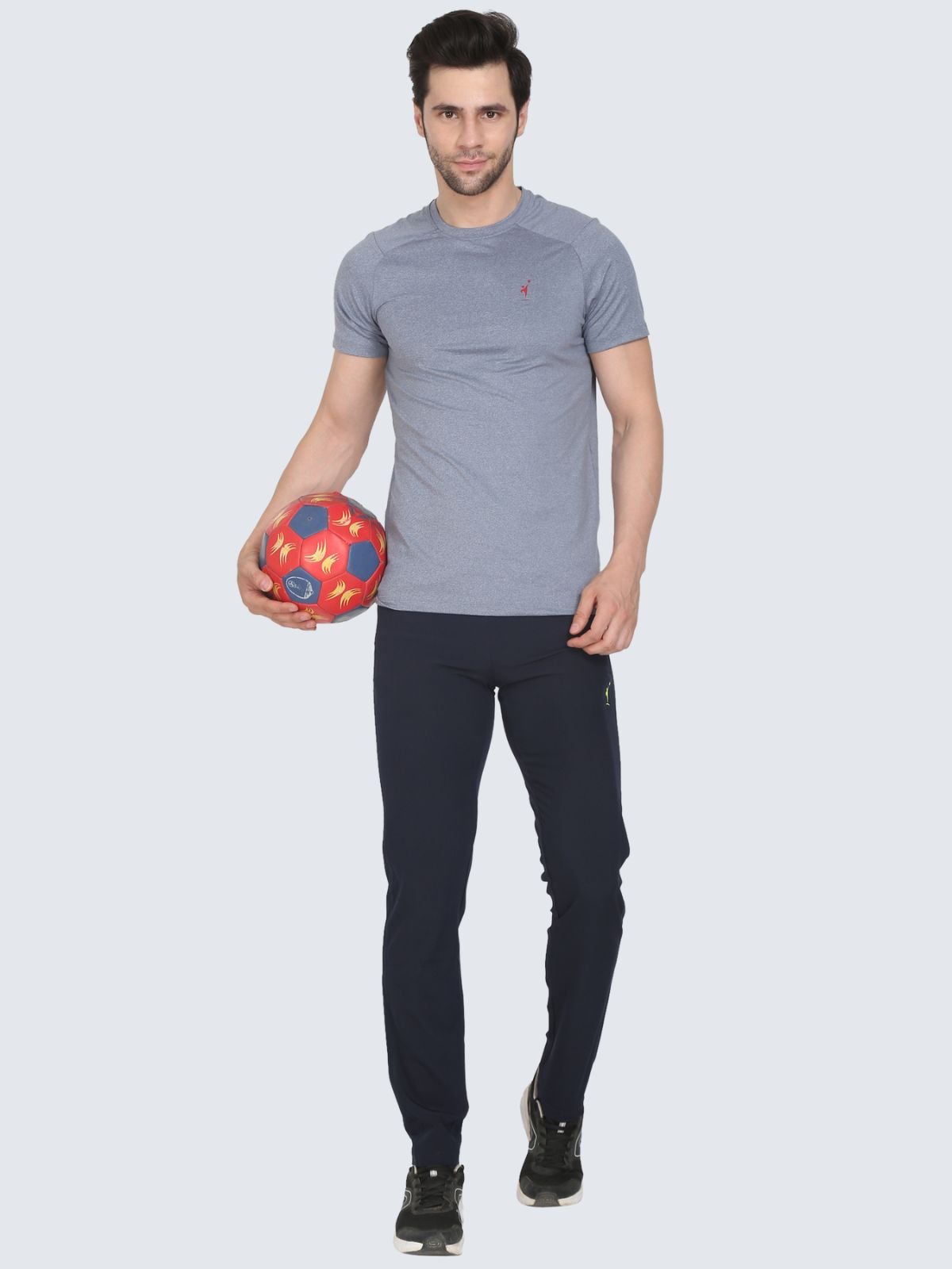 Full-body male model in grey cool N comfort tee wearing Lite Plain navy athletic pants holding a red soccer ball on a white background